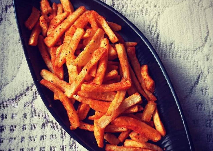 a black plate filled with french fries on top of a white tablecloth covered table