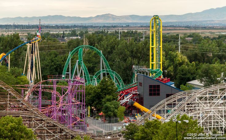 an amusement park with several roller coasters and trees in the foreground, mountains in the background