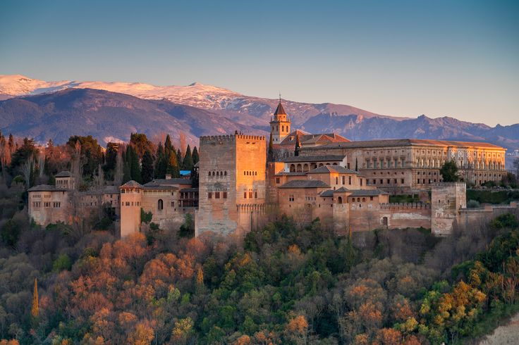 an old castle sits on top of a hill with trees and mountains in the background