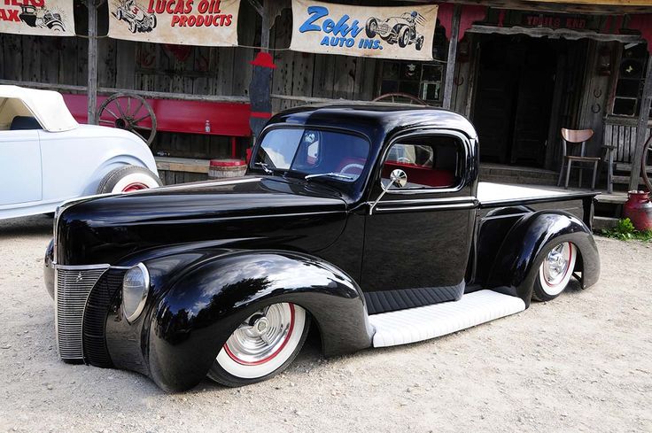 an old black car parked in front of a building with signs on the side of it