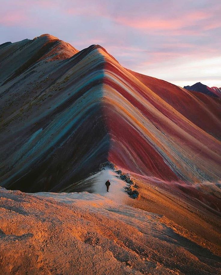 a man standing on top of a mountain next to a rainbow colored slope at sunset