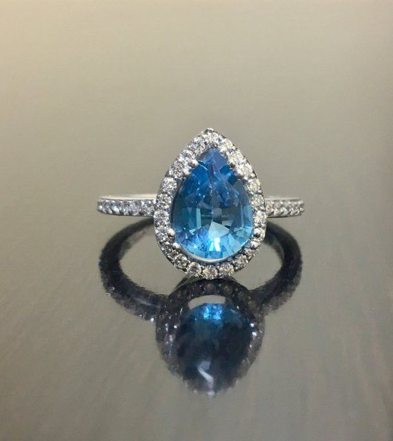 a pear shaped blue topaz and diamond ring on a reflective surface with reflection in the foreground