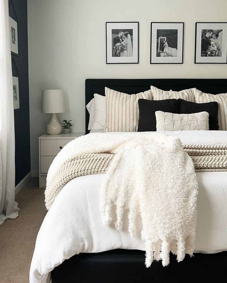 a bed with white blankets and black pillows in a bedroom next to pictures on the wall