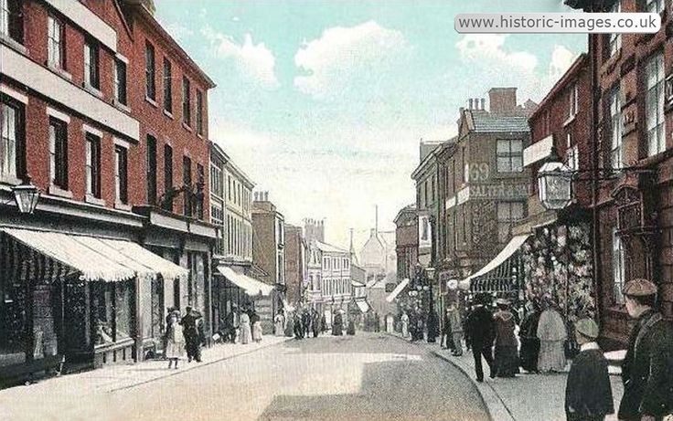 an old photo of people walking down the street in front of buildings and shops on both sides