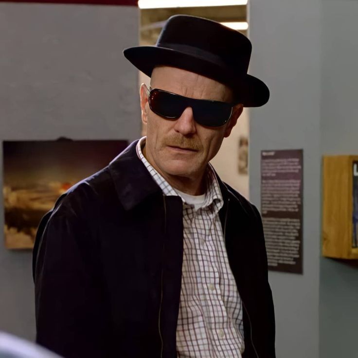 an older man wearing sunglasses and a hat in a room with pictures on the wall