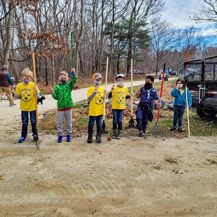 several children in yellow shirts holding up baseball bats on dirt ground with trees and grass behind them