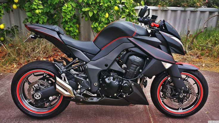 a black motorcycle parked on top of a parking lot next to a green bush and tree