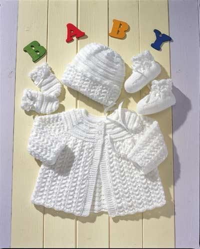 a knitted baby outfit and booties are laid out on a white wooden surface