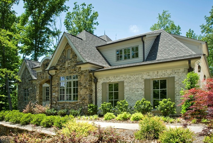 a stone house with lots of windows and bushes around it's front yard area