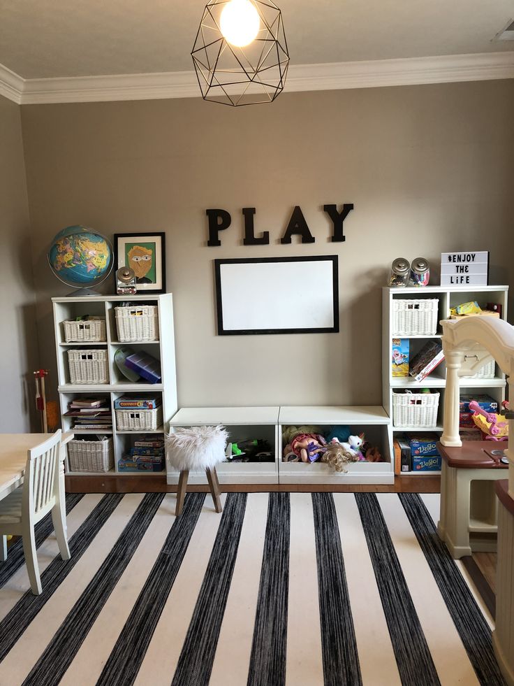 a playroom with toys and bookshelves on the wall, striped rug in front of it