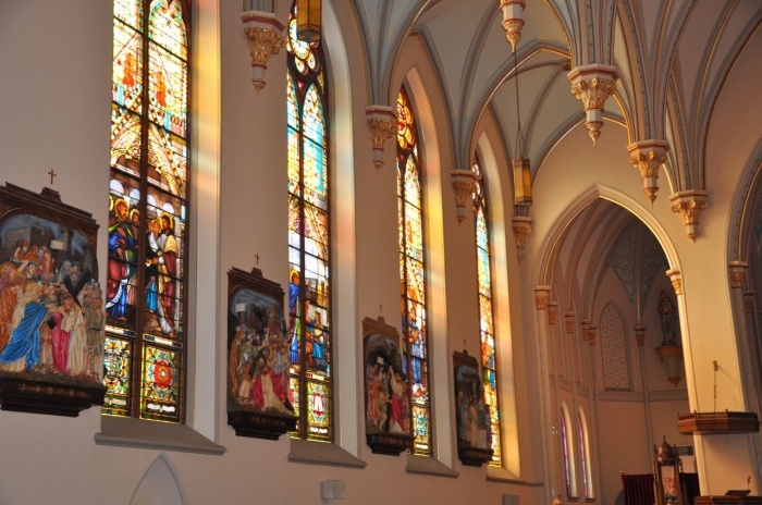 the interior of a large church with stained glass windows and paintings on the side wall