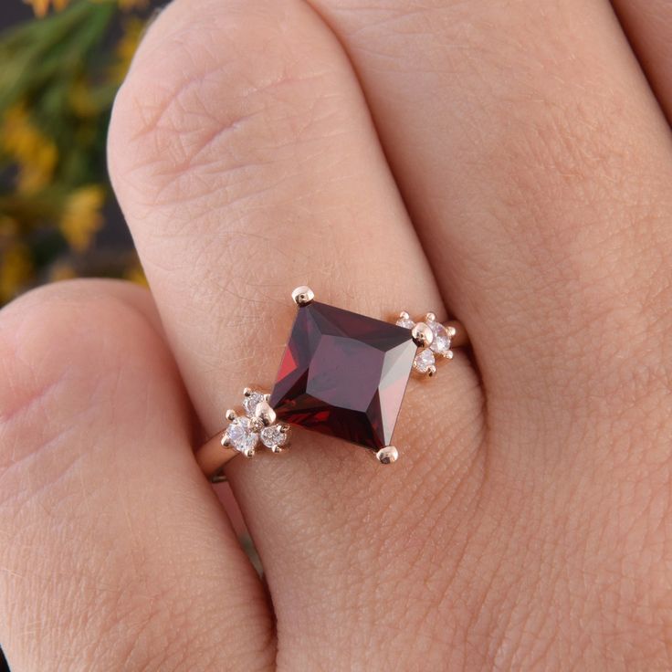 a woman's hand with a ring on it that has a red stone in the middle