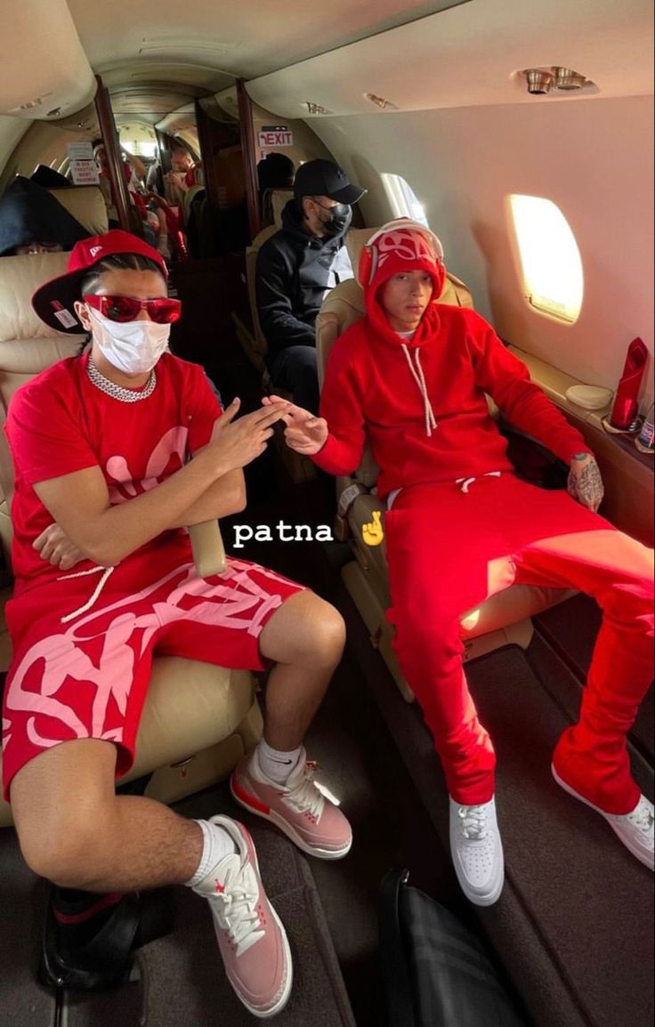 two people in red and white outfits sitting on an airplane with one person wearing a face mask