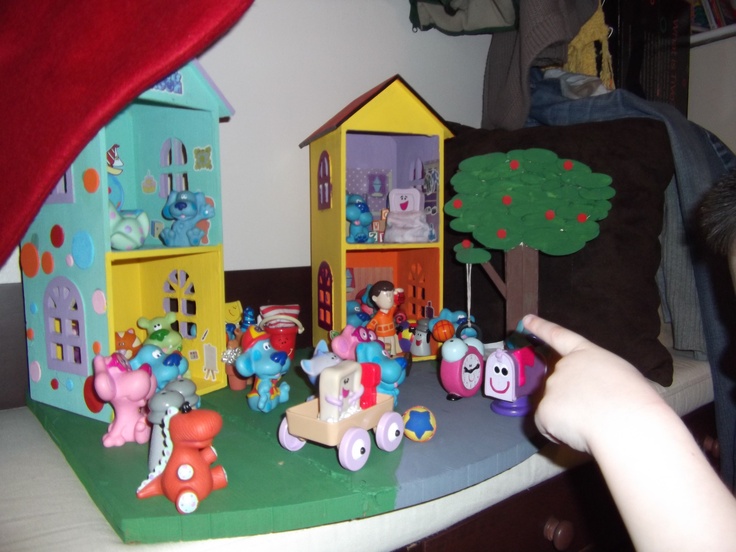 a child pointing at a toy house with many toys on the table next to it