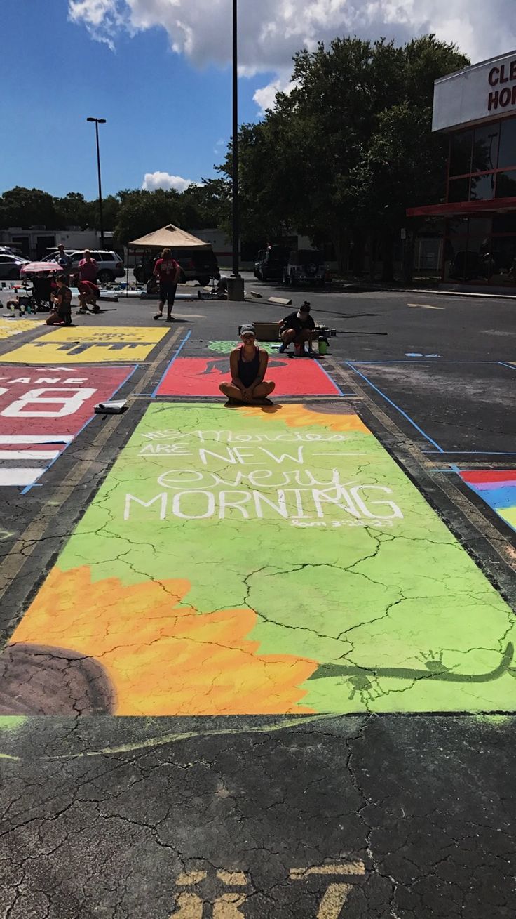 a person sitting on the ground in front of a painted road with words and trees