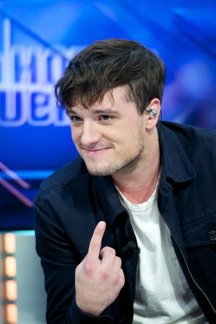 a man with ear buds on his ears pointing to the side while sitting in front of a news desk