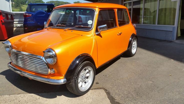 an orange mini car parked in front of a building with other small cars behind it