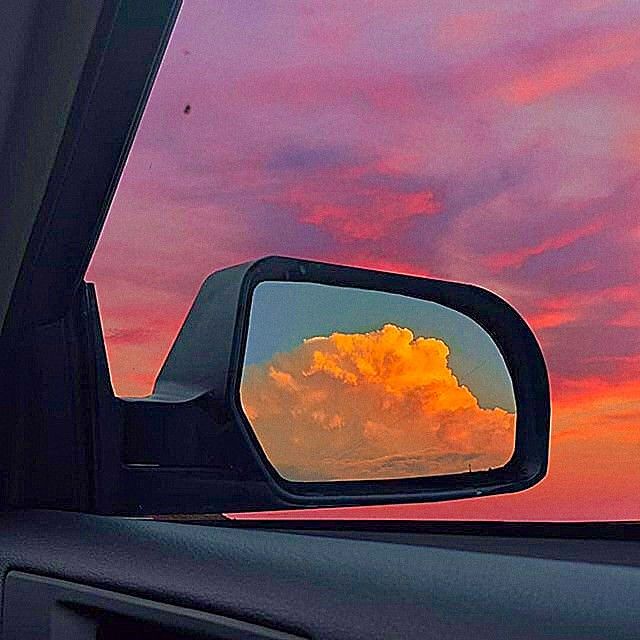 the clouds are reflected in the rear view mirror as the sun is setting behind them