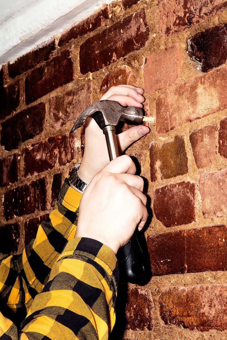 a person is holding a shoe in their right hand while standing against a brick wall