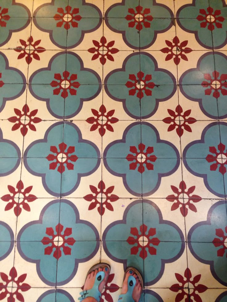 someone's feet on the floor in front of a tiled wall with red and blue flowers