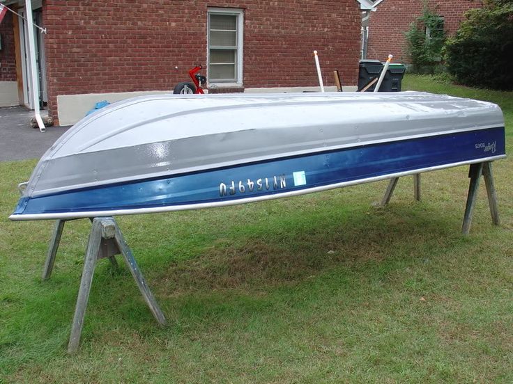 a silver and blue boat sitting on top of a grass covered field next to a building