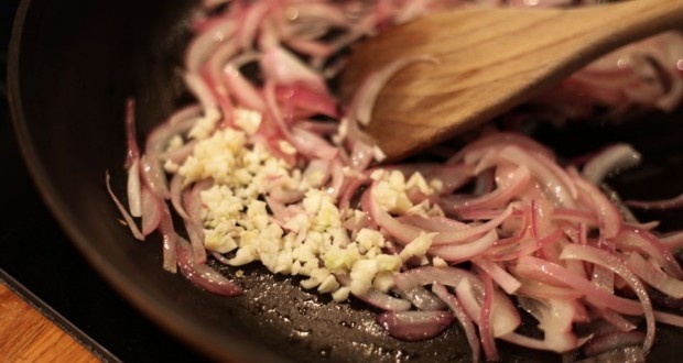 onions being cooked in a frying pan with a wooden spoon