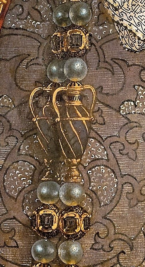 an ornate gold and silver broochle with pearls on it's sides, sitting on a fabric background