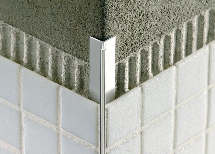 the corner of a bathroom wall with white tiles and silver metal bars sticking out of it