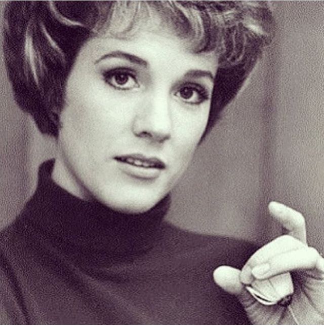 a black and white photo of a woman with short hair pointing to the side while wearing a turtle neck sweater