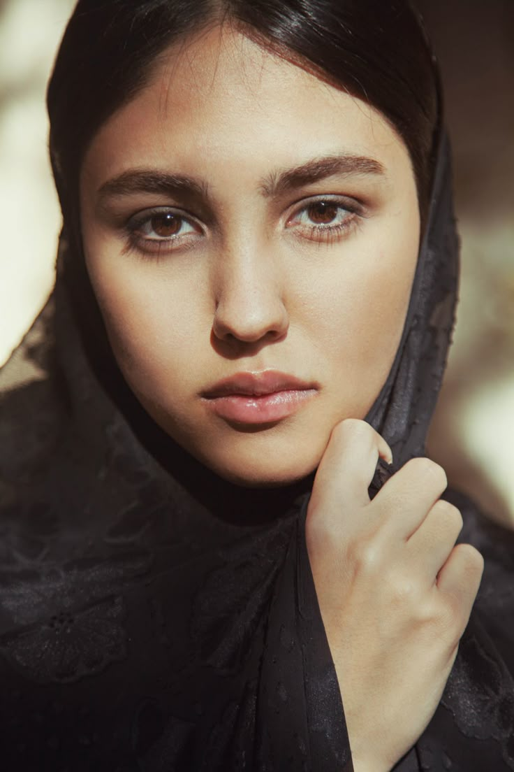 a woman wearing a black hijab and holding her hand on her chin looking at the camera