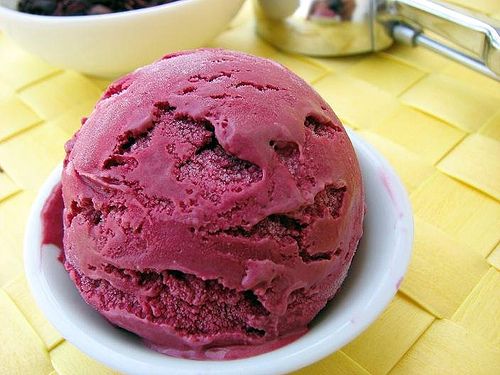 a bowl filled with red ice cream next to a spoon on a yellow place mat