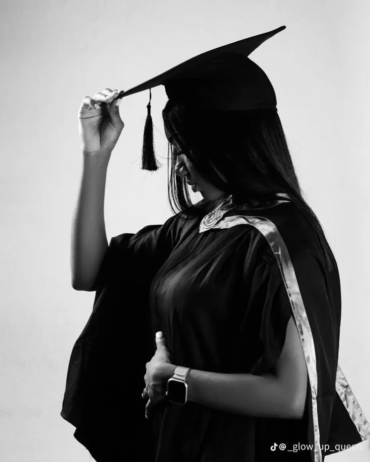 a woman wearing a graduation gown and holding her cap in the air with one hand