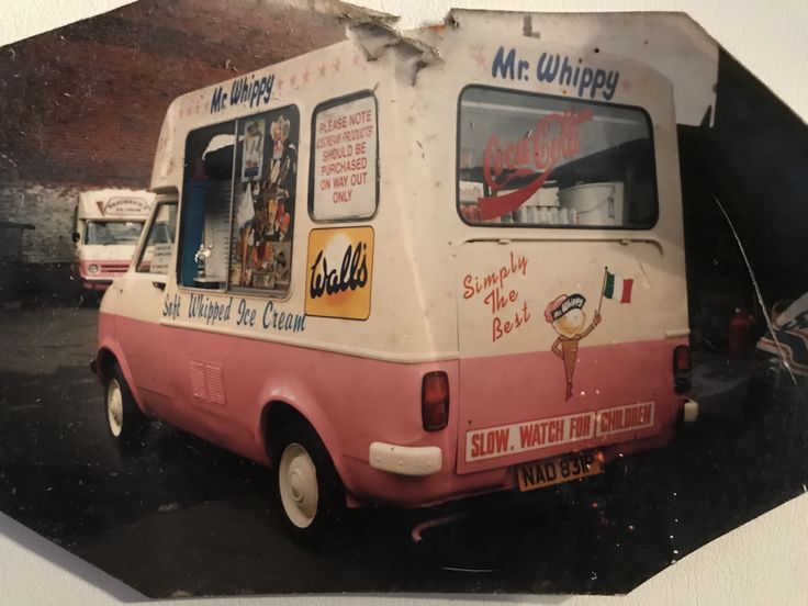 an old pink and white ice cream truck parked in a parking lot next to other vehicles