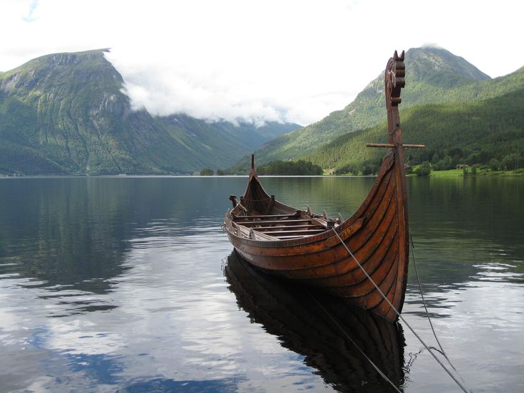 an old wooden boat sitting in the middle of a lake with mountains in the background