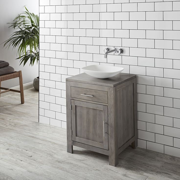 a bathroom sink sitting next to a white tiled wall with a potted plant in the corner