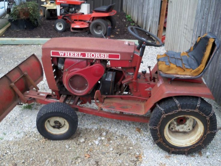 an old red tractor parked in front of a fenced off area with two lawn mowers