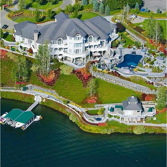 an aerial view of a large house with a boat on the water in front of it