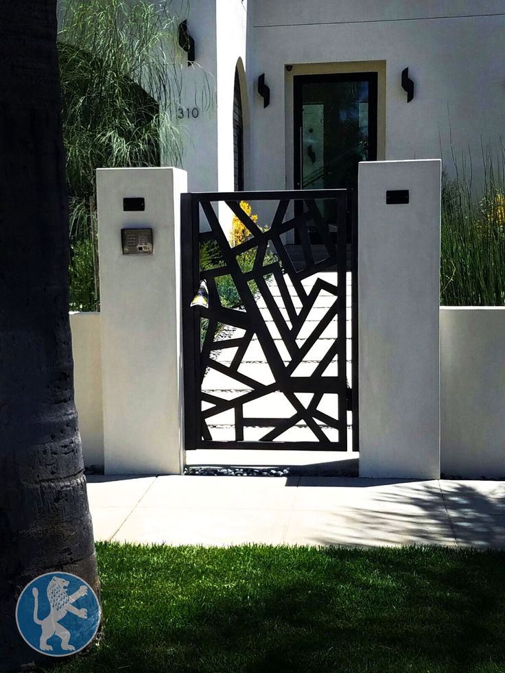 an open gate in front of a white house with palm trees and grass around it