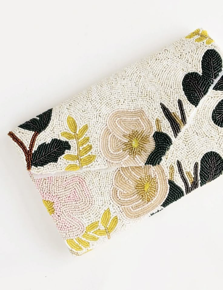 an embroidered clutch bag with flowers and leaves on the front, sitting on a white surface