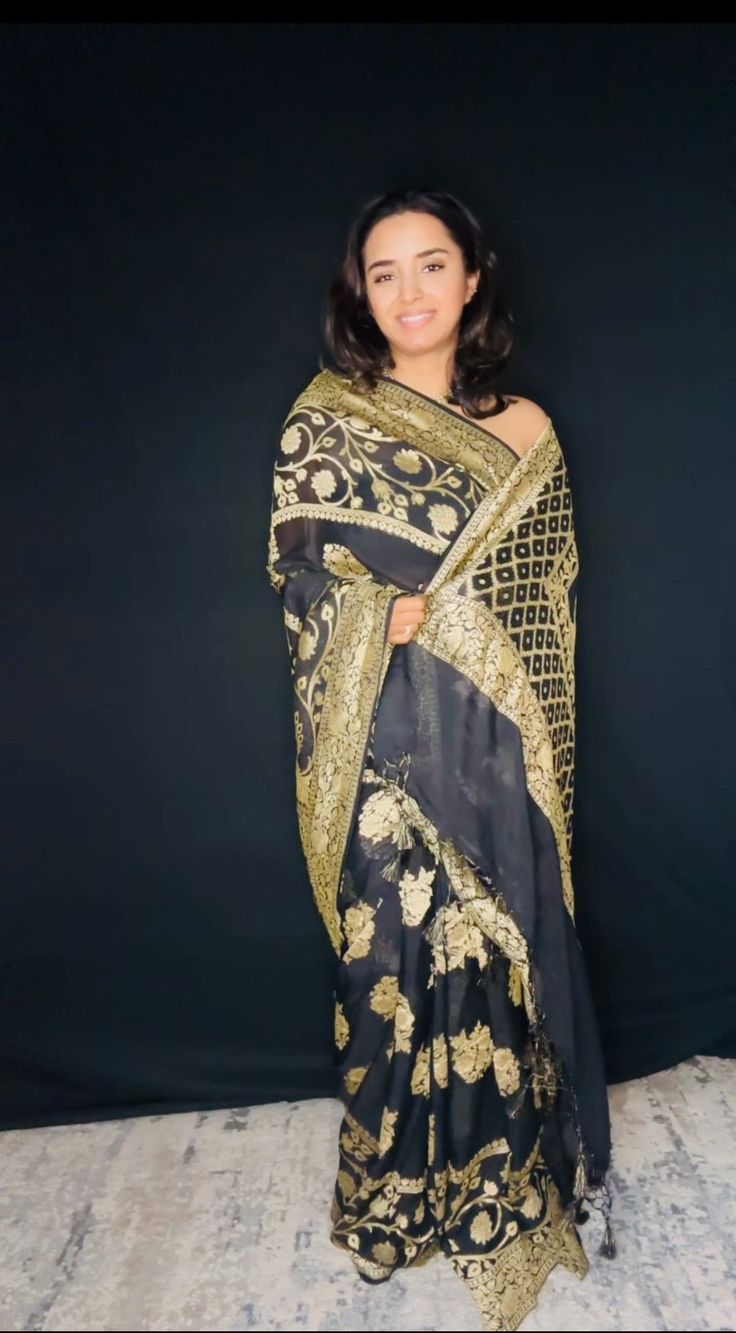 Indulge in timeless elegance with our exquisite Black Banarasi Khaddi Georgette Saree, adorned with lustrous gold zari. This masterpiece seamlessly blends traditional artistry with contemporary sophistication. Crafted from the finest Khaddi Georgette, the saree drapes effortlessly, creating a graceful and ethereal silhouette. The classic black hue serves as the perfect canvas for the intricate gold zari work, which adds a touch of opulence and glamour. Handwoven by skilled artisans, this saree showcases the rich heritage of Banaras. The delicate interplay of light and shadow created by the gold zari on the black base results in a mesmerizing visual effect. Perfect for evening soirees, weddings, or any special occasion where you desire to make a lasting impression. Fabric: Pure Khaddi Georg Gold Brocade Pre-draped Saree With Zari Work, Gold Brocade Pre-draped Saree With Zari Weaving, Gold Pre-draped Saree With Traditional Patterns For Festivals, Elegant Meenakari Pre-draped Saree For Festivals, Bollywood Style Brocade Pre-draped Saree For Designer Wear, Elegant Gold Pre-draped Saree For Festivals, Gold Pre-draped Jamawar Saree With Zari Work, Traditional Gold Pre-draped Saree With Self Design, Semi-stitched Brocade Pre-draped Saree With Zari Work