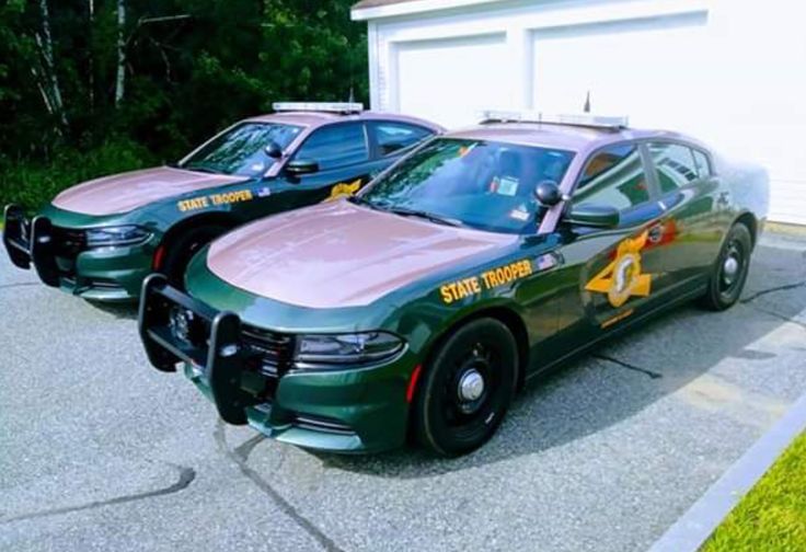 two green police cars parked in front of a garage next to a white car with yellow lettering on it