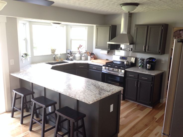 a kitchen with black cabinets and white counter tops, stainless steel appliances and stools