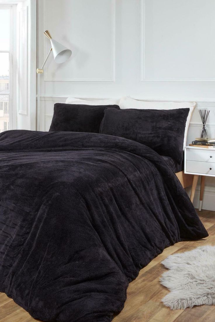 a black comforter set on a wooden floor next to a white table and lamp