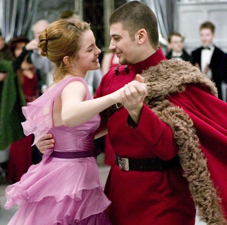 a man in a red suit and woman in a pink dress dance together at an event