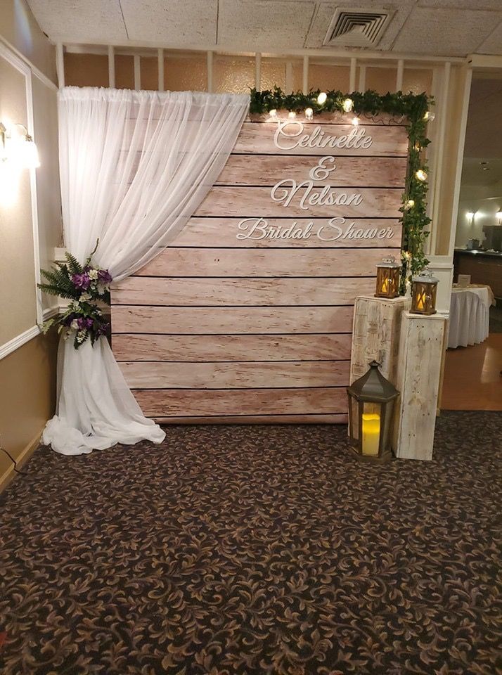 a wooden sign with white drapes and flowers on it in front of a wedding ceremony backdrop