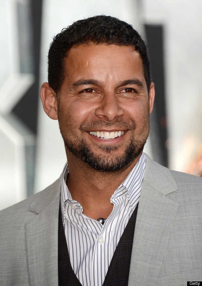 a smiling man in a gray suit and striped shirt is looking at the camera with a smile on his face