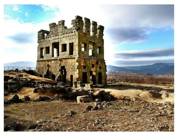 an old stone building sitting on top of a hill with mountains in the back ground