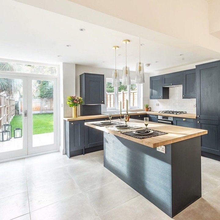 a large kitchen with blue cabinets and an island in the middle is shown, along with glass doors that lead out to a back yard