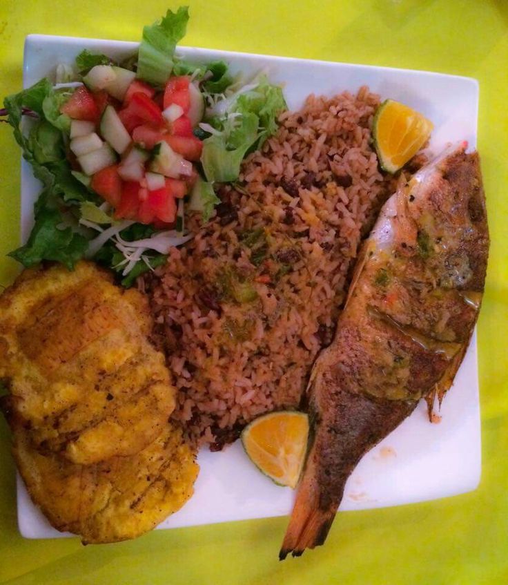 a white plate topped with fish next to rice and veggies on a yellow table