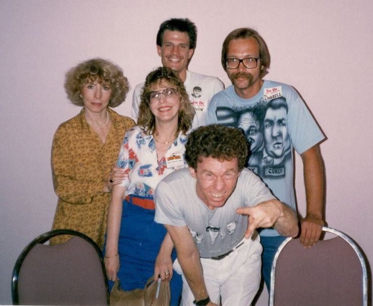 a group of people standing next to each other in front of a table with chairs